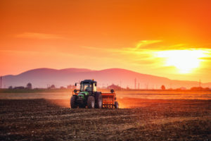 Farmer with tractor seeding crops at field on sunset